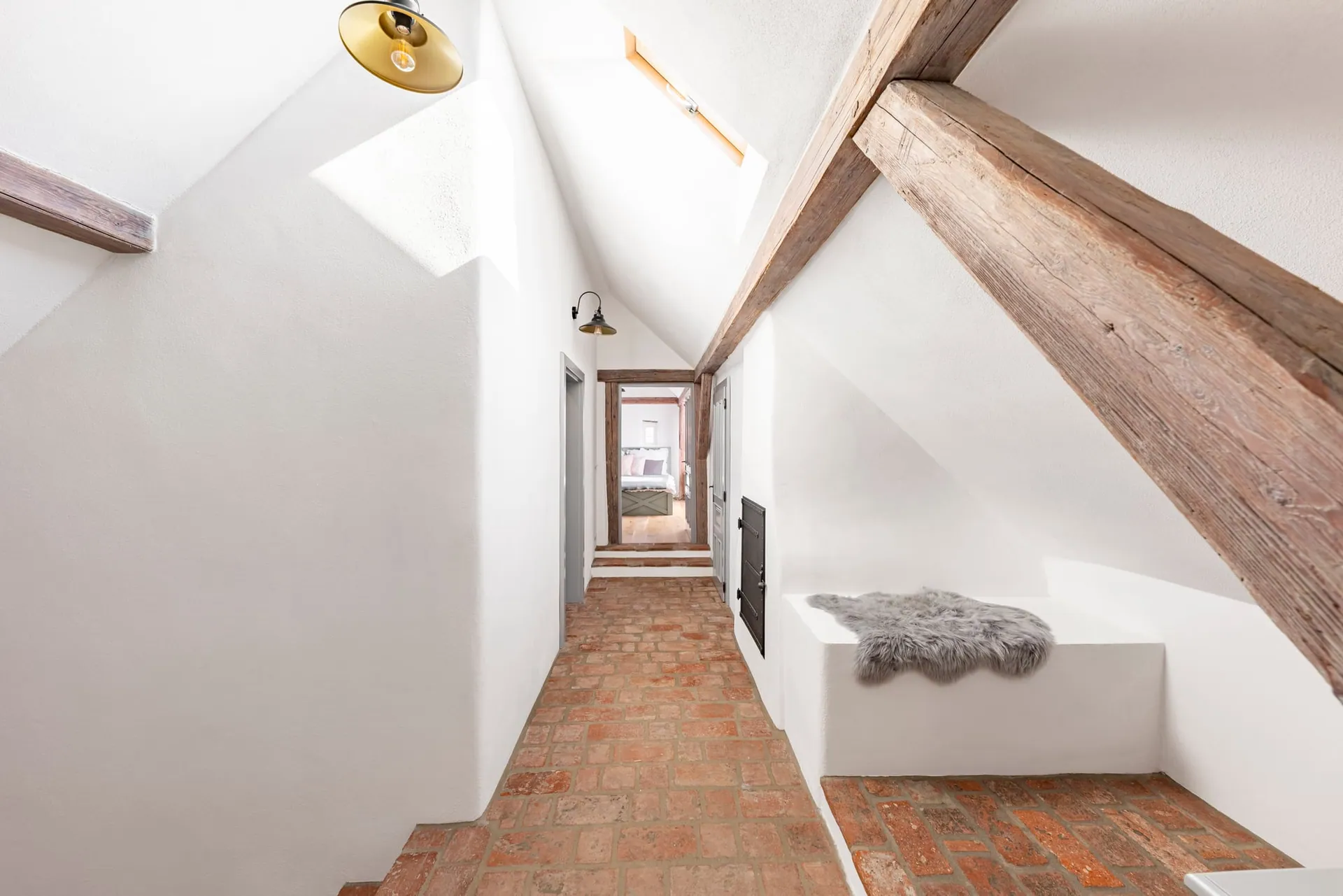Brick-floored attic landing beneath timber beams, leading to an open bedroom door.