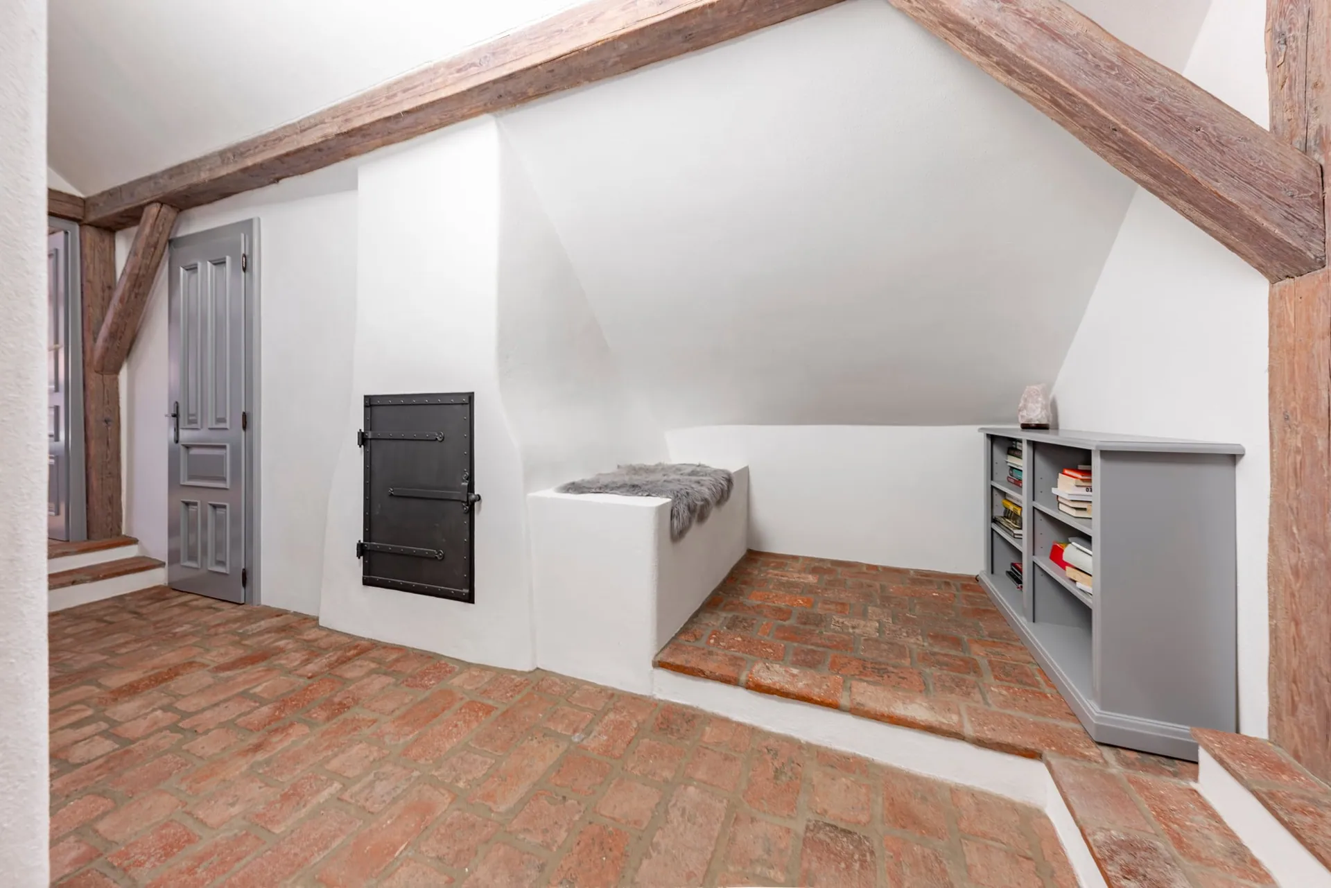 Attic landing with a whitewashed chimney breast, small iron door, plastered bench and low bookcase.