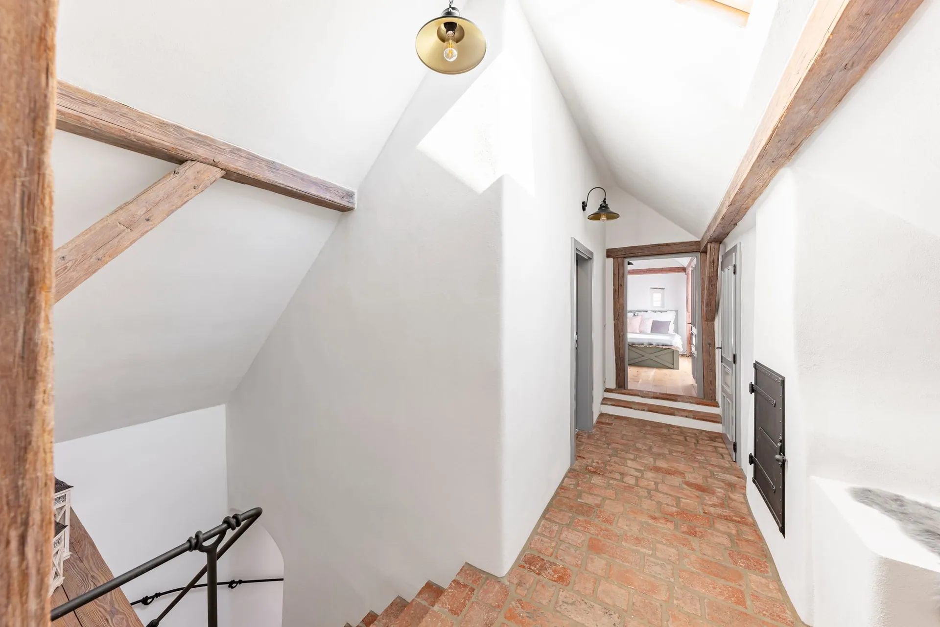 Top of the staircase with a wrought-iron railing, opening onto the brick-floored attic landing.