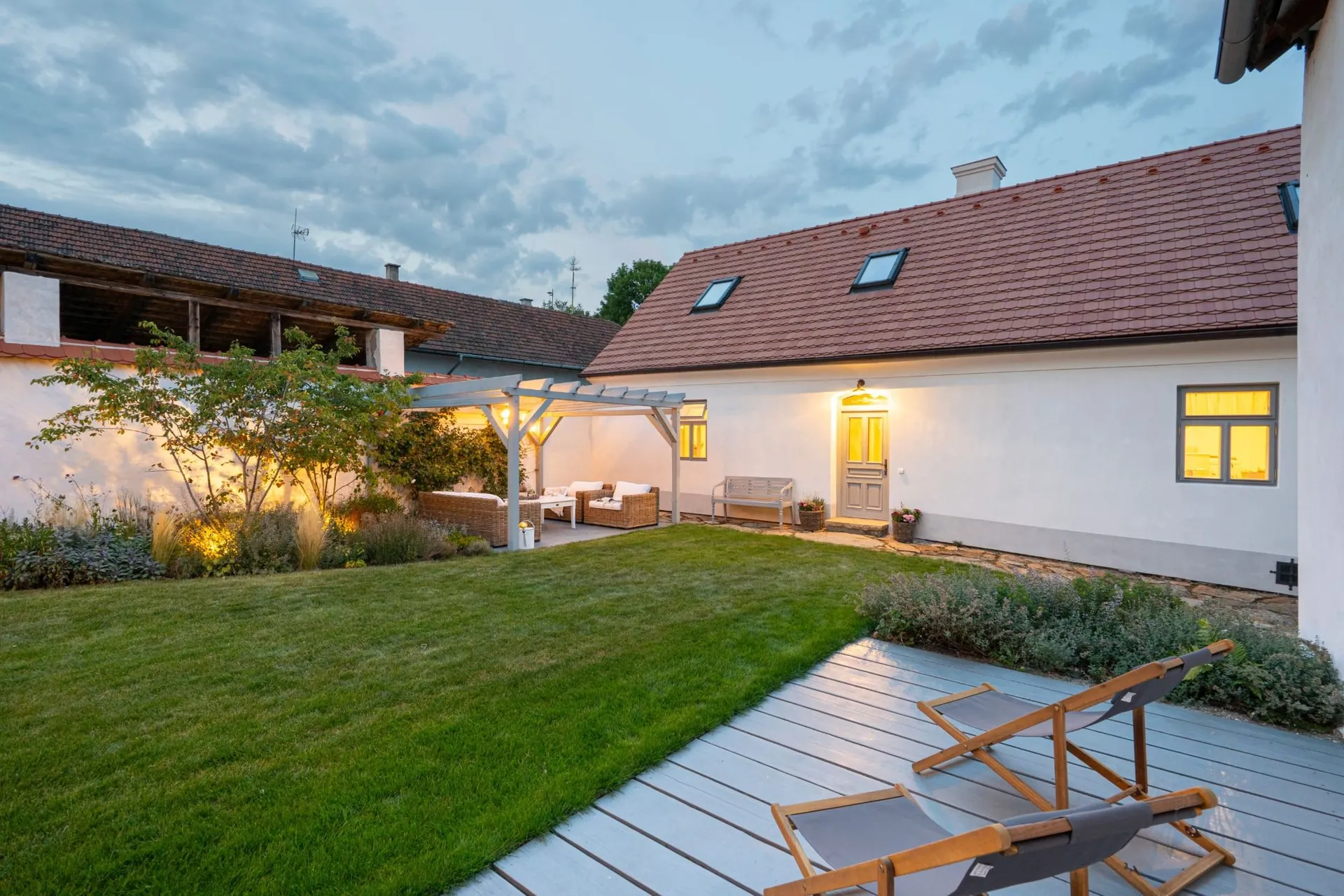 The main house, the lawn and deckchairs on the terrace at dusk