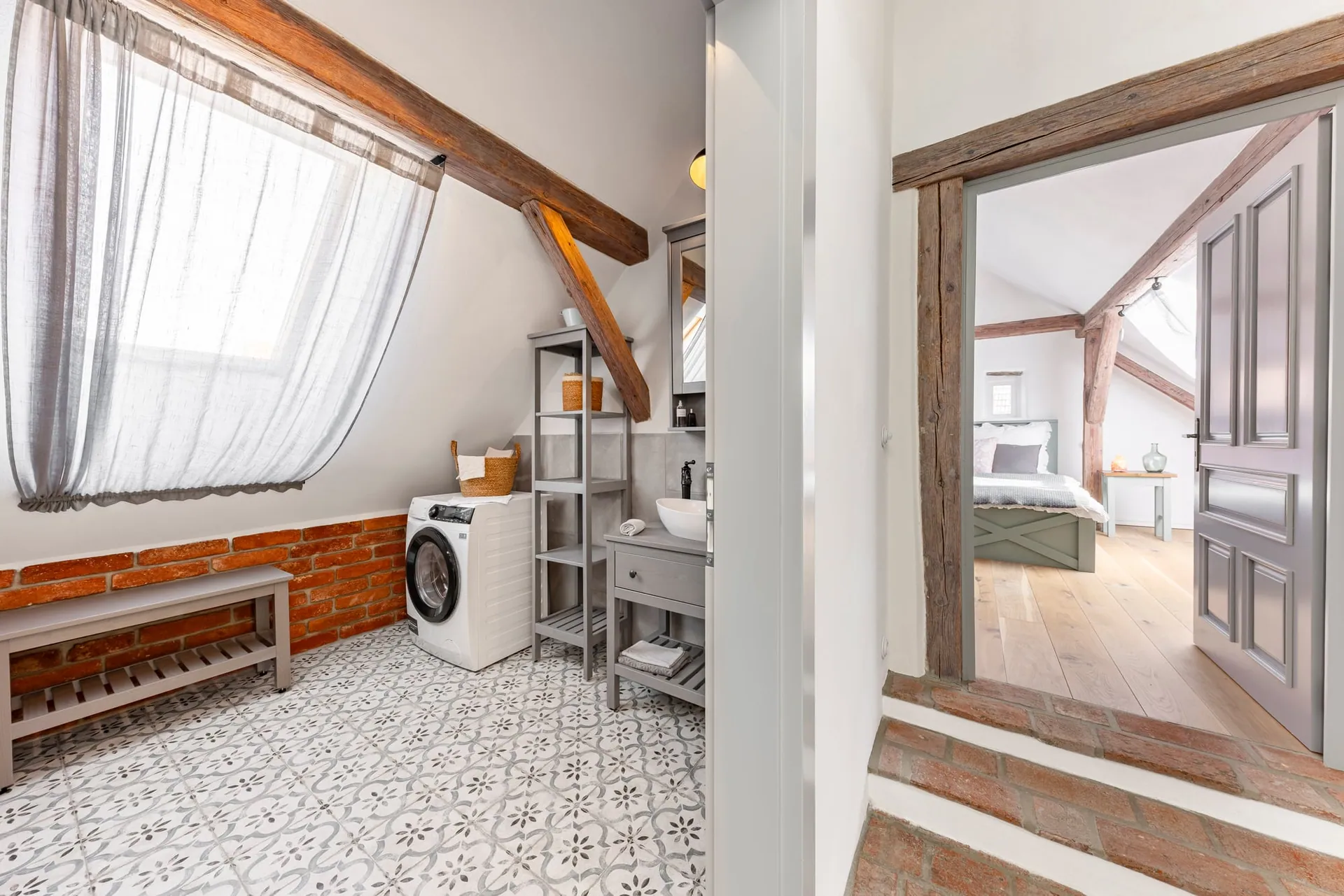Attic bathroom with timber beams and a washing machine, beside an open door to a bedroom.