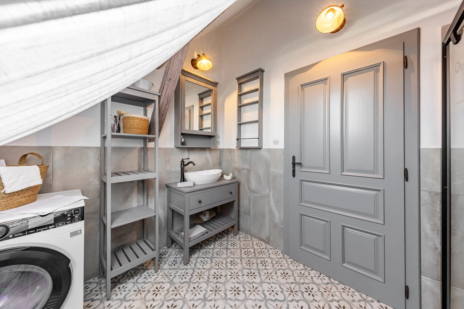 Attic bathroom with a basin on a grey wooden washstand, mirror cabinet and panelled grey door.
