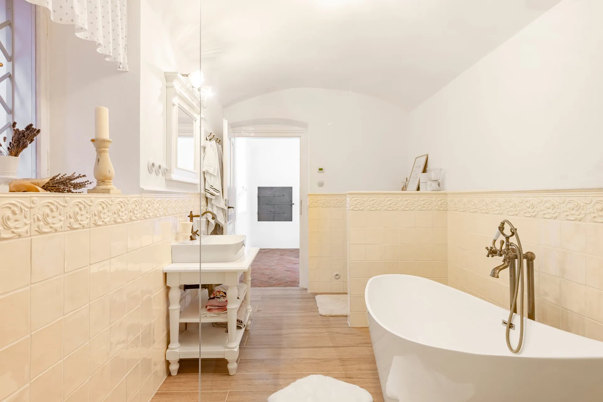 Bathroom with a vaulted ceiling, cream tiles, a freestanding bath and a basin on a washstand.