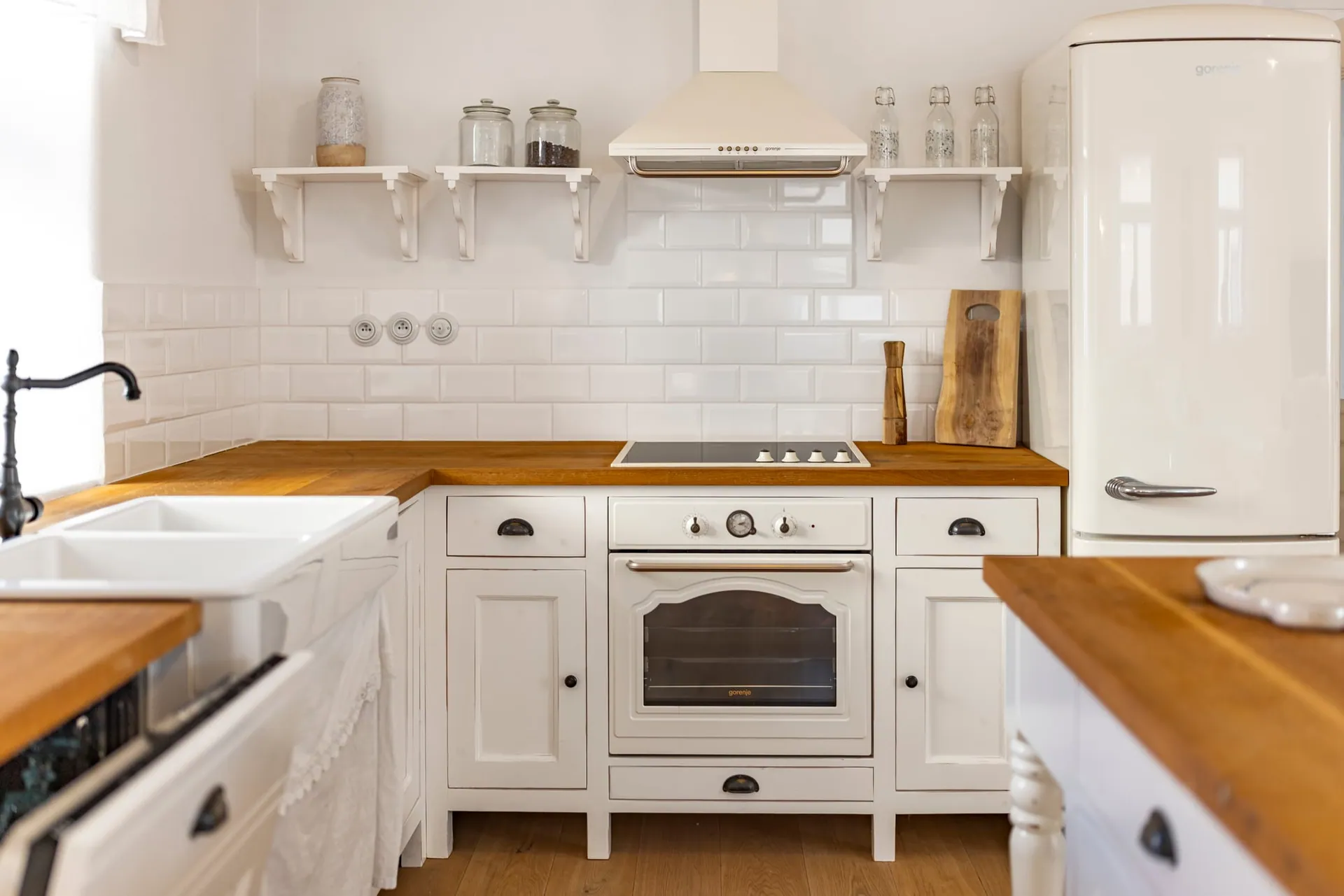 White kitchen units with a wooden worktop, cream retro-style oven, cooker hood and fridge.