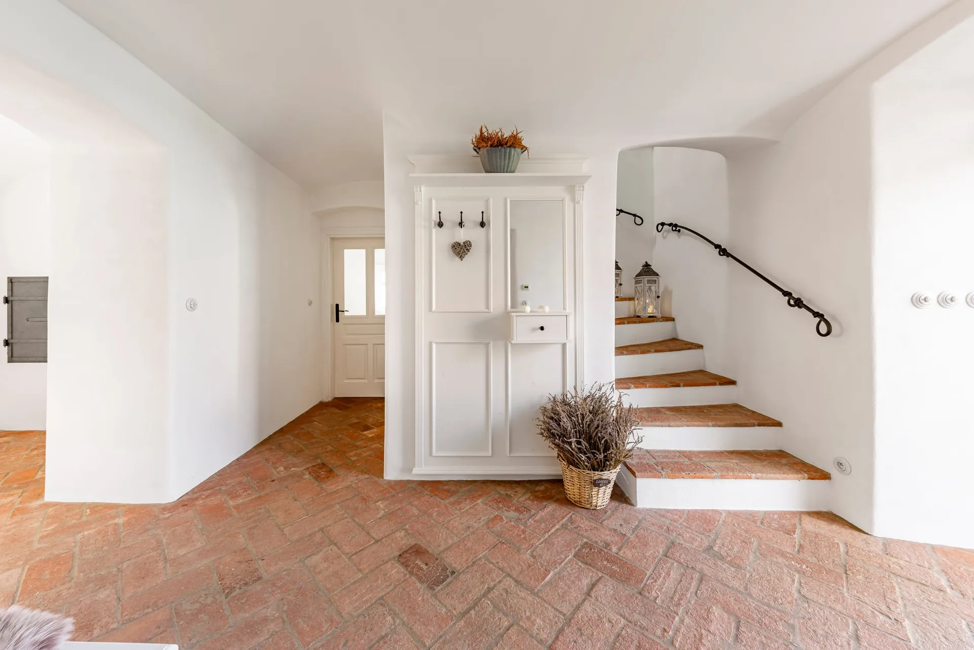 Entrance hall with a herringbone brick floor, white panelled hall stand and staircase with a wrought-iron handrail.