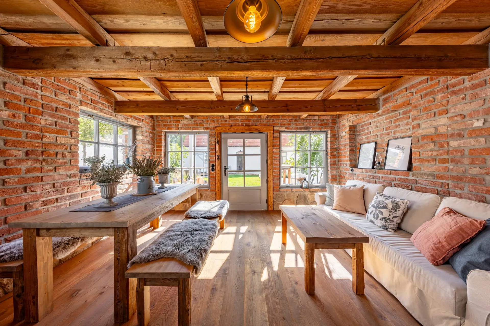 Garden house with a long table, fleece-covered benches and a sofa against the brick walls.