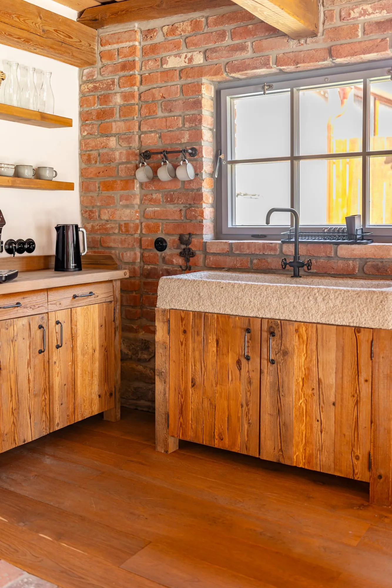 Garden-house kitchenette with wooden cupboards, a stone sink and an exposed brick wall.
